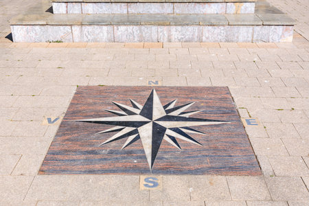 Compass rose on stone pavement indicating cardinal directions outdoors.