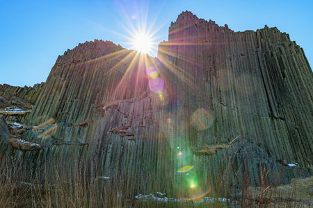 Sunlit basalt cliffs with lens flare and clear sky.の写真素材