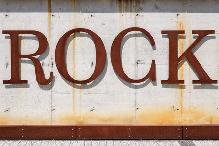 Large rusty metal rock letters on weathered concrete wall.の写真素材