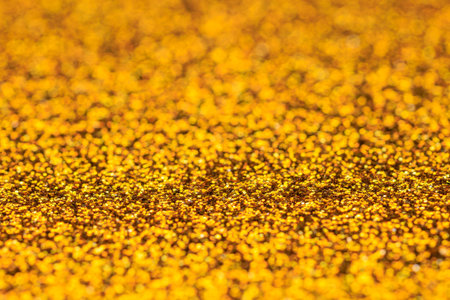 A close up of gold glitter with a lot of texture. The gold glitter is scattered all over the...