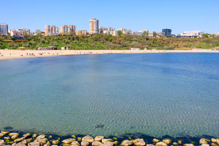 Serene urban beachscape with clear blue water and distant city buildings.の写真素材