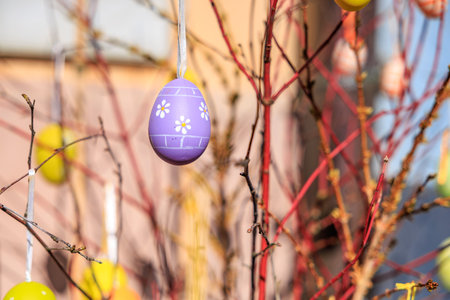 A tree with many Easter eggs hanging from its branches. The eggs are painted and have a purple and...