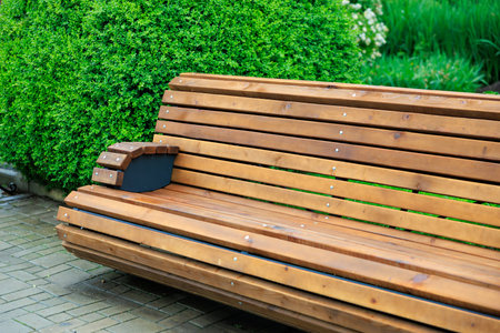 Wooden park bench on stone pathway with green shrubs in background.の写真素材
