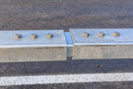 Close-up of metal guardrail with bolts on asphalt road surface.の写真素材