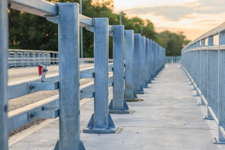 Empty blue metal bridge railings at sunset with trees and sky in background.の写真素材