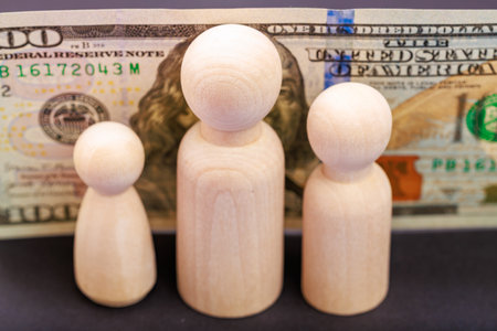 Wooden figures in front of hundred dollar bill symbolizing economy and finance.