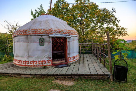 A round tent with a red and white design sits on a wooden deck. The tent is open, kyrgyz authentic nomadic yurtの写真素材
