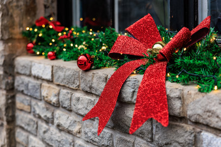 Festive red bow and green garland with lights on brick wall during christmas season.の写真素材