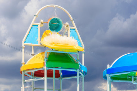 A colorful water slide with a rainbow colored roof. The sky is cloudy and the water is splashingの写真素材