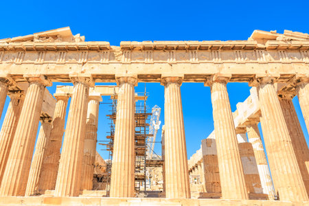 The columns of the Parthenon are being repaired. The sky is clear and blue. The columns are made of...