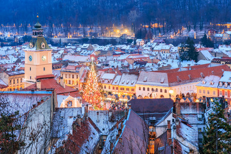 A city with a tall clock tower and a Christmas tree in the center. The city is lit up at night,...