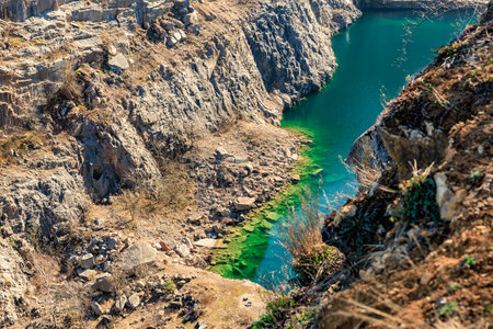 Scenic rocky quarry with vibrant turquoise water and green algae in natural sunlight.