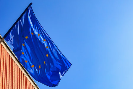 European union flag waving against clear blue sky on brick building.