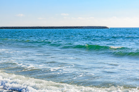 Tranquil ocean waves on a sunny day with clear skies and stone breakwater.