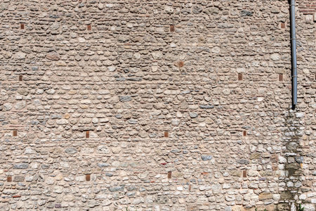 Stone wall with textured surface and vertical pipe on side.の写真素材