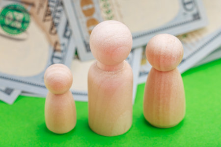 Wooden figures with dollar bills on green background symbolizing finance and economy.の写真素材