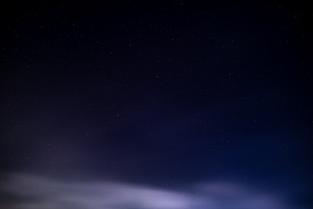 Starry night sky with dark clouds and distant stars.