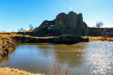 Basalt rock formation by tranquil lake under clear blue sky.