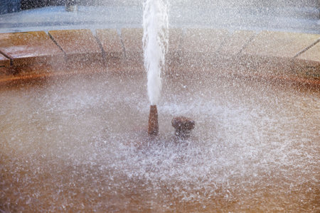 Close-up view of splashing water fountain with stone base in sunlit setting.の写真素材