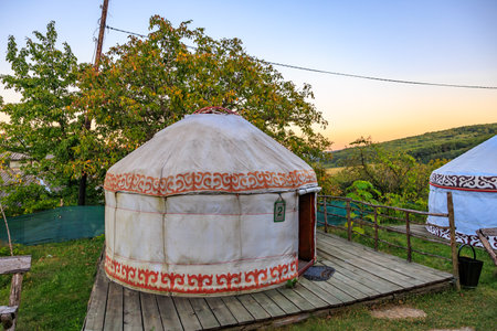 A round tent with a red and white design sits on a wooden deck. The tent is open, kyrgyz authentic...