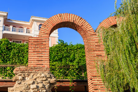 Brick arch ruins with lush greenery and residential building in the background.の写真素材