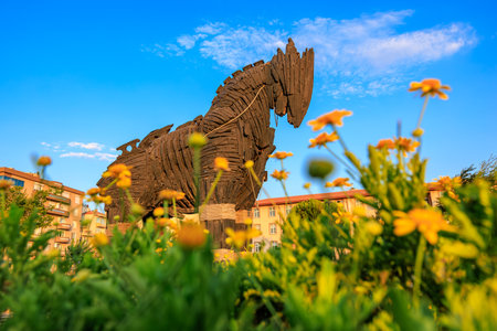 Trojan horse sculpture in city park with flowers and vibrant blue sky.の写真素材