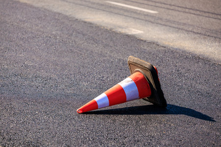 Traffic cone on asphalt road surface under bright sunlight.の写真素材