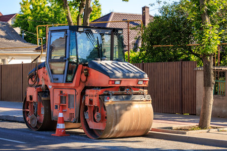 Orange construction steamroller parked on urban street for roadwork maintenance.の写真素材