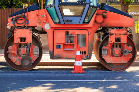 Orange road roller and traffic cone on urban street for construction and maintenance.の写真素材