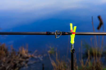 Fishing rod on stand with blue lake background and bright yellow holder.の写真素材