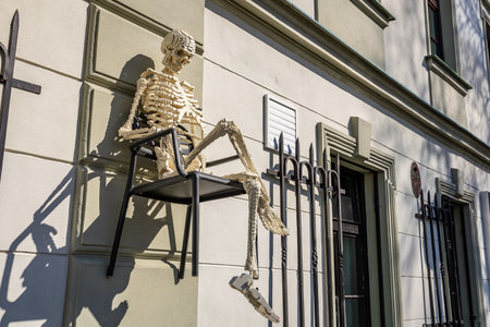 Skeleton sculpture sitting on chair attached to building facade in sunlit urban setting.. March 22, 2025, Kutna Hora, Czech Republic.のeditorial素材