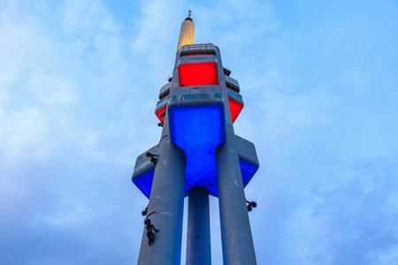 Modern communication tower with blue and red illumination against cloudy sky. March 22, 2025 Prague Czechia.のeditorial素材