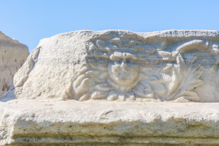 Ancient stone carving of mythical face with sun motif against blue sky. Authentic ancient Smyrna...