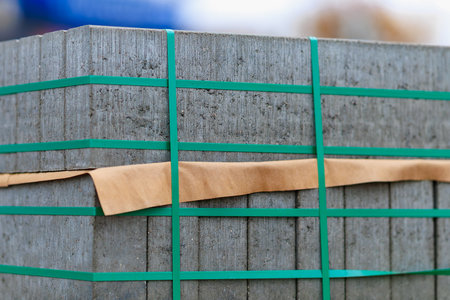 Heavy concrete blocks are neatly stacked and secured with green straps at a construction site. They are prepared for upcoming building projects and nearby equipment.の写真素材