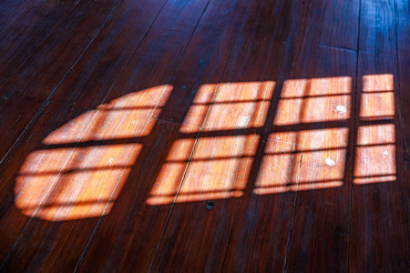 Warm sunlight filtering through window casting grid shadows on wooden floor.の写真素材