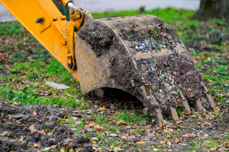 Excavator bucket in muddy park setting with green grass and leaves.の写真素材