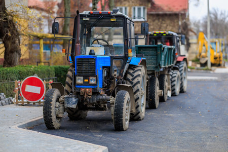 Blue tractor on urban street with trailers during road construction.の写真素材