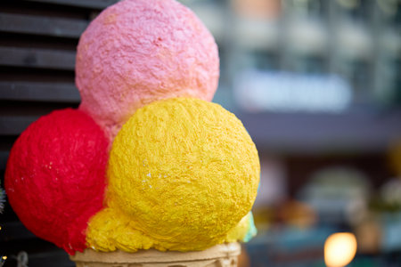 Colorful ice cream sculpture with pink, red, and yellow scoops in urban setting.