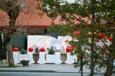 Festive outdoor dining igloos with holiday decorations in urban setting. December 13, 2025 Sinaia Romania.のeditorial素材