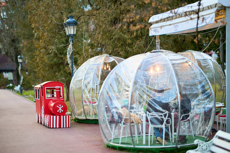 Transparent dining bubbles with red toy train in outdoor park setting. December 13, 2025 Sinaia Romania.のeditorial素材