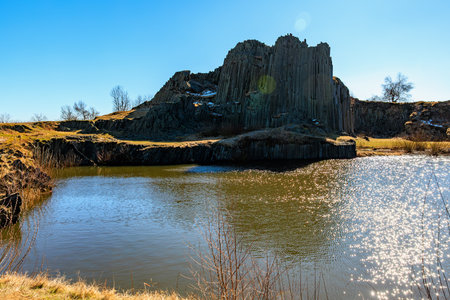 Scenic basalt rock formation with tranquil lake in sunlit landscape.