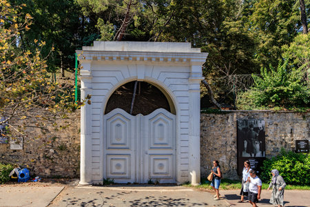 Historic arched gateway with diverse individuals walking in park setting. August 12, 2025 Istanbul Turkey.のeditorial素材