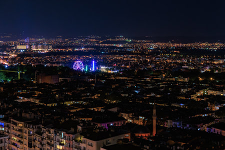 Night view of ferris wheel illuminating cityscape with vibrant lights and buildings. August 9, 2025, 2 Bursa Turkey.のeditorial素材
