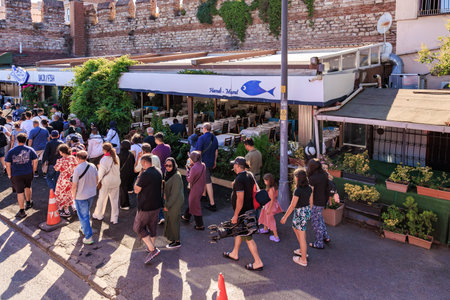 Bustling street scene with diverse crowd in urban setting near outdoor cafe. August 12, 2025...