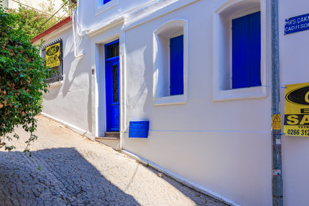White mediterranean building with blue doors and shutters on cobblestone street. August 3, 2025, Ayvalik, Turkey.のeditorial素材