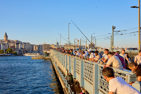 Galata bridge fishing scene at sunset with crowd of diverse people. August 10, 2025, Istanbul Turkey.のeditorial素材