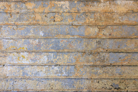 Weathered concrete wall with peeling paint in beige and blue tones.