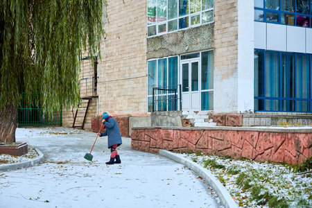 Elderly woman sweeping snow outside building in winter urban scene.の写真素材