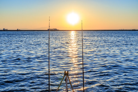 Sunset reflection on the sea with fishing poles and distant ships.の写真素材