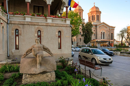 Historic church and sculpture in southern europe urban setting with romanian flag. May 3, 2025 Constanta Romania.のeditorial素材